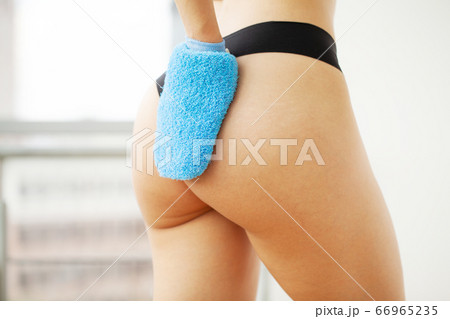 Woman's arm holding blue dry brush to top of her buttocks, cellulite treatment and dry brushing. 66965235