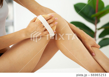 Woman's arm holding dry brush to top of her leg, cellulite treatment and dry brushing. 66965253