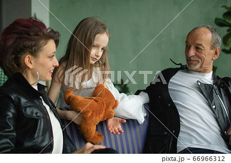 Family portrait of adult daughter, little granddaughter and senior grandfather in loft room with houseplants. Man and woman are wearing black leather jackets in punk style, generation concept Family portrait of adult daughter, little granddaughter and senior grandfather in loft room with houseplants. Man and woman are wearing black leather jackets in punk style, generation concept 66966312