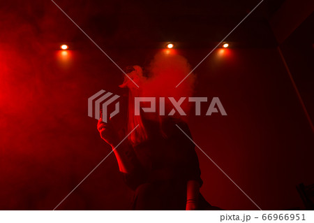 Girl model smokes vape in red light. 66966951