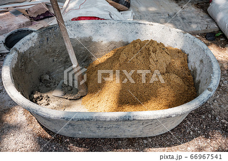 Hoe mixing cement, sand and water in bucket 66967541