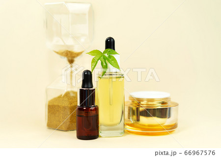 Glass bottles with herbal CBD oil, THC tincture, cream, hemp leaf and hourglass on pastel beige 66967576