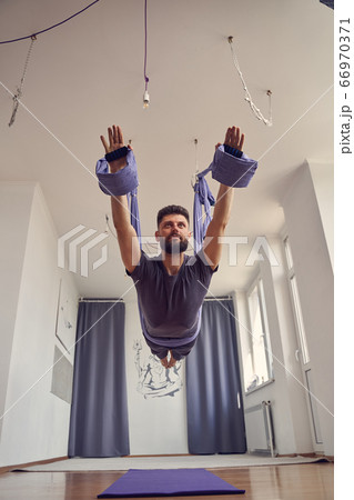 Handsome bearded man practicing aerial yoga in studio Handsome bearded man practicing aerial yoga in studio 66970371