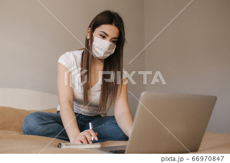 Young woman in mask use laptop on the bed. Female working during quarantine in bedroom. Student study at home. Stay at home Young woman in mask use laptop on the bed. Female working during quarantine in bedroom. Student study at home. Stay at home 66970847
