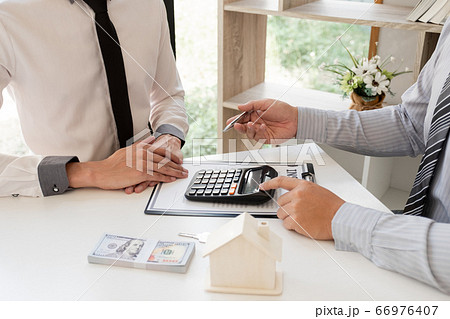A real estate agent with House model is talking to clients about buying home insurance. Home insurance concept A real estate agent with House model is talking to clients about buying home insurance. Home insurance concept 66976407