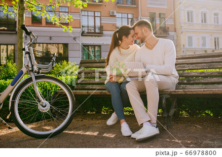 Woman and man with map sitting on bench touching faces Woman and man with map sitting on bench touching faces 66978800