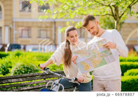 Woman sitting on bicycle and man with map standing nearby. Woman sitting on bicycle and man with map standing nearby. 66978807