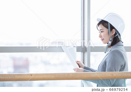 ビジネス　ヘルメットをかぶって図面を見る女性 66979254