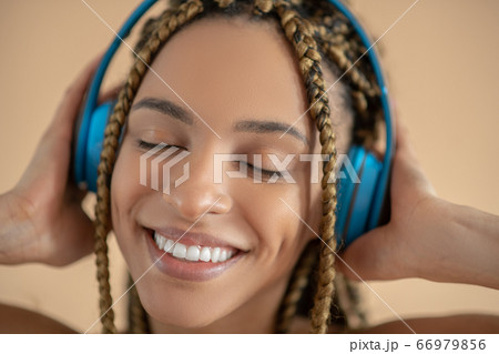 Smiling young African American female in blue headphones, listening to music with closed eyes Smiling young African American female in blue headphones, listening to music with closed eyes 66979856