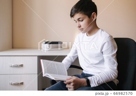 Young boy sitting by the desk and read the book. Study at home during quarantine Young boy sitting by the desk and read the book. Study at home during quarantine 66982570