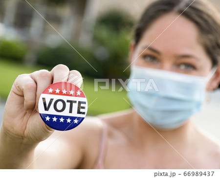 Portrait of women wearing face mask holding Vote button Portrait of women wearing face mask holding Vote button 66989437
