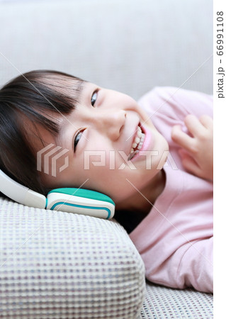 ヘッドフォンで音楽を聴きながらソファに寝転ぶ女の子 66991108