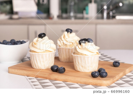Homemade cupcakes with blueberry and vanilla cream on wooden board. Home kitchen background. Homemade cupcakes with blueberry and vanilla cream on wooden board. Home kitchen background. 66996160