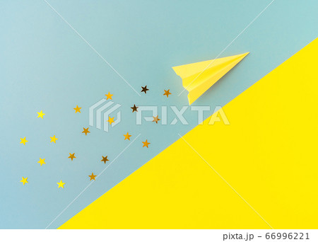 Top view of yellow paper plane with golden star shaped confetti trail on blue and yellow background. Minimalist flat lay image with copy space. 66996221