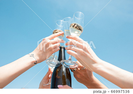Seasonal feast at beach resort. Close up hands of friends celebrating, resting, having fun, clinking glasses on sky background 66997536