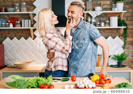 Beautiful young couple is feeding each other and smiling while cooking in kitchen at home Beautiful young couple is feeding each other and smiling while cooking in kitchen at home 66998910