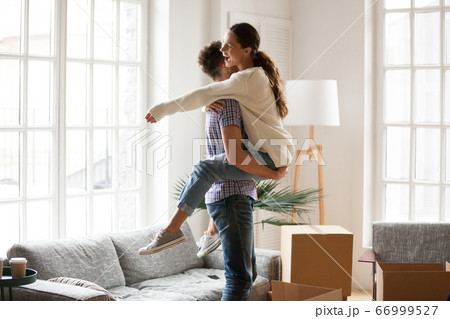 Excited couple celebrating moving day, man lifting embracing hap 66999527