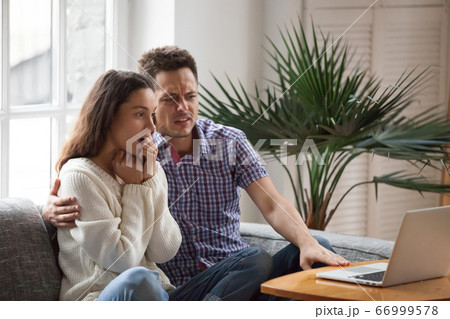 Scared man embracing shocked woman watching horror film on lapto Scared man embracing shocked woman watching horror film on lapto 66999578