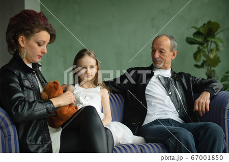 Family portrait of adult daughter, little granddaughter and senior grandfather in loft room with houseplants. Man and woman are wearing black leather jackets in punk style, generation concept Family portrait of adult daughter, little granddaughter and senior grandfather in loft room with houseplants. Man and woman are wearing black leather jackets in punk style, generation concept 67001850