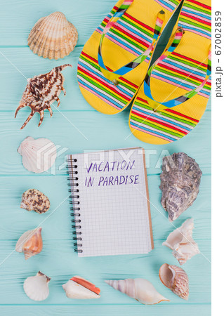 Along the perimeter are different sea shells and bright sandals in the corner on turquoise background. Along the perimeter are different sea shells and bright sandals in the corner on turquoise background. 67002859