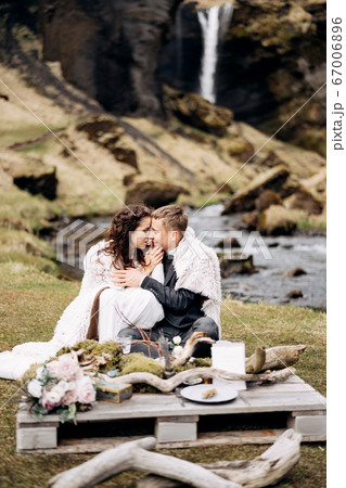 Destination Iceland wedding, near Kvernufoss waterfall. A wedding couple sits on the banks of a mountain river, at a table for a wedding dinner, made of a wooden pallet painted with moss and snags 67006896