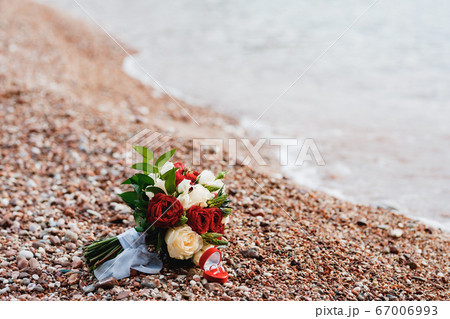 bridal bouquet of white, read and cream roses, ornithogalum, eryngium with white ribbons on the beach near water and wedding rings bridal bouquet of white, read and cream roses, ornithogalum, eryngium with white ribbons on the beach near water and wedding rings 67006993