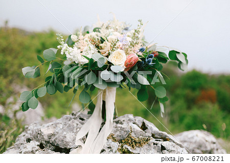 bridal bouquet of white and cream roses, branches of eucalyptus tree, protea, eryngium, delphinium and white ribbons on the stone bridal bouquet of white and cream roses, branches of eucalyptus tree, protea, eryngium, delphinium and white ribbons on the stone 67008221