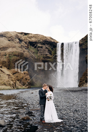 Destination Iceland wedding. Wedding couple near Skogafoss waterfall. The bride and groom are hugging near the river. 67008248