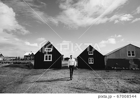 Destination Iceland wedding. A man in a white shirt walks between two wooden black houses. Black and white photography. Destination Iceland wedding. A man in a white shirt walks between two wooden black houses. Black and white photography. 67008544