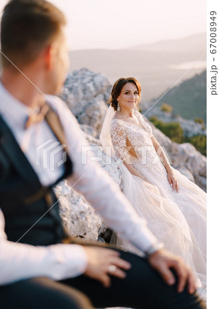 A wedding couple on top of a mountain in the Bay of Kotor, the bride smiles to the groom at sunset. Fine-art destination wedding photo in Montenegro, Mount Lovchen. 67008949