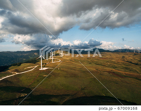 Aerial photo from a drone - a series of huge high wind turbines along a road on a hill among the mountains in Montenegro. Aerial photo from a drone - a series of huge high wind turbines along a road on a hill among the mountains in Montenegro. 67009168