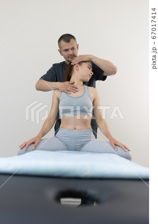 Chiropractic treatment - young woman sitting on the couch and the doctor working with her neck Chiropractic treatment - young woman sitting on the couch and the doctor working with her neck 67017414