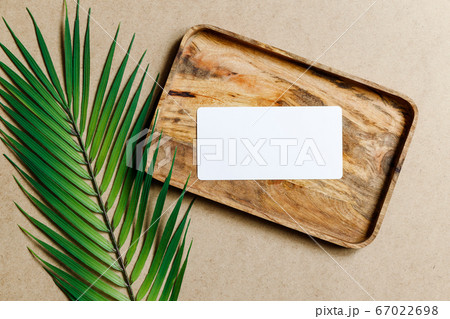 Top view of a blank paper sheet card on a wooden tray with palm leaf. Summer mockup for business template, copy space. Top view of a blank paper sheet card on a wooden tray with palm leaf. Summer mockup for business template, copy space. 67022698