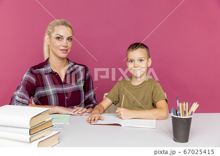 Homework together at quarantine concept. Mother with kid sitting at the desk with books and studying. 67025415