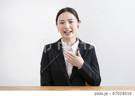 ワイヤレスヘッドホンをつけて話すカメラ目線のスーツ姿の若い女性 67028016