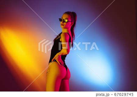 Beautiful seductive girl in fashionable swimsuit on disco bicolored neon studio background in neon light. Summer, resort, fashion and weekend concept Beautiful seductive girl in fashionable swimsuit on disco bicolored neon studio background in neon light. Summer, resort, fashion and weekend concept 67029745