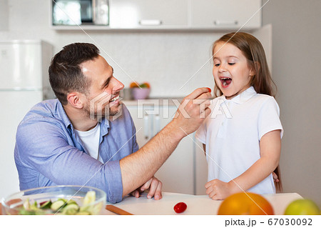 Father Feeding Little Daughter Preparing Dinner In Kitchen At Home Father Feeding Little Daughter Preparing Dinner In Kitchen At Home 67030092