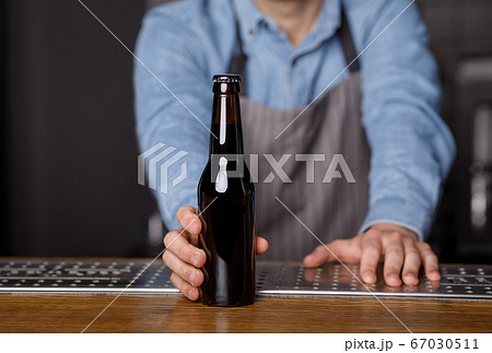 Evening in pub. Bartender gives to client bottle of beer at bar Evening in pub. Bartender gives to client bottle of beer at bar 67030511