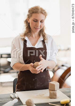 Female potter shaping piece of clay at the table. Woman making ceramic item. Pottery working, handmade and creative skills at arts studio. Female potter shaping piece of clay at the table. Woman making ceramic item. Pottery working, handmade and creative skills at arts studio. 67040473