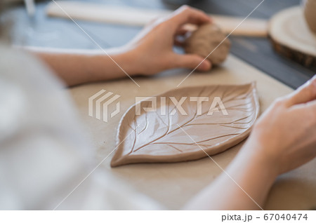Female hands holding stick and making ornament on decorative product. Clay master moulding clay on a pottery and ceramics workshop. Female hands holding stick and making ornament on decorative product. Clay master moulding clay on a pottery and ceramics workshop. 67040474