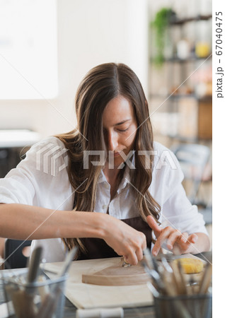 Woman working with clay with her hands and loop cutting tool close up at a pottery workshop. Woman working with clay with her hands and loop cutting tool close up at a pottery workshop. 67040475