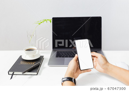 Man hands holding mobile phone with laptop computer on table. 67047300