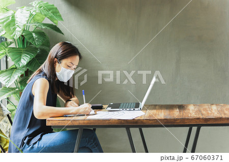 Woman wearing face mask for prevention while working on paperwork with laptop on table. 67060371