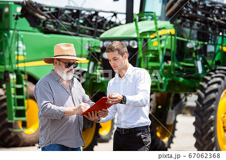 A farmer with a tractor, combine at a field in sunlight. Confident, bright colors 67062368