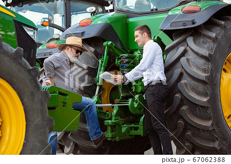 A farmer with a tractor, combine at a field in sunlight. Confident, bright colors A farmer with a tractor, combine at a field in sunlight. Confident, bright colors 67062388
