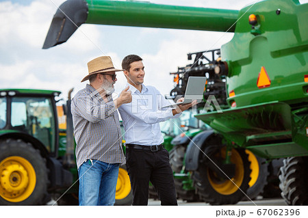 A farmer with a tractor, combine at a field in sunlight. Confident, bright colors A farmer with a tractor, combine at a field in sunlight. Confident, bright colors 67062396