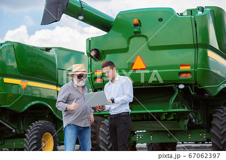 A farmer with a tractor, combine at a field in sunlight. Confident, bright colors A farmer with a tractor, combine at a field in sunlight. Confident, bright colors 67062397