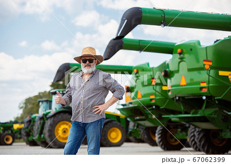 A farmer with a tractor, combine at a field in sunlight. Confident, bright colors 67062399