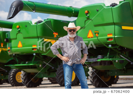 A farmer with a tractor, combine at a field in sunlight. Confident, bright colors 67062400