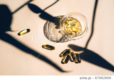 Capsules fish oil omega-3 in glass cup with a shadow of monstera leaves in the sunlight on the beige background. Capsules fish oil omega-3 in glass cup with a shadow of monstera leaves in the sunlight on the beige background. 67062600